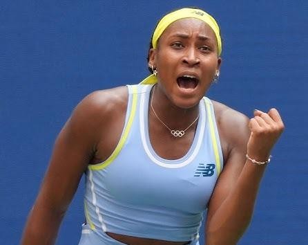 Coco Gauff w dynamicznym ujęciu na korcie tenisowym, podczas serwisu lub forhendu, z widoczną piłką i zamazanym tłem stadionu.
