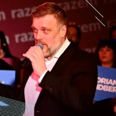 Adrian Zandberg w interakcji z ludźmi podczas wiecu politycznego, uśmiechnięty i zaangażowany.