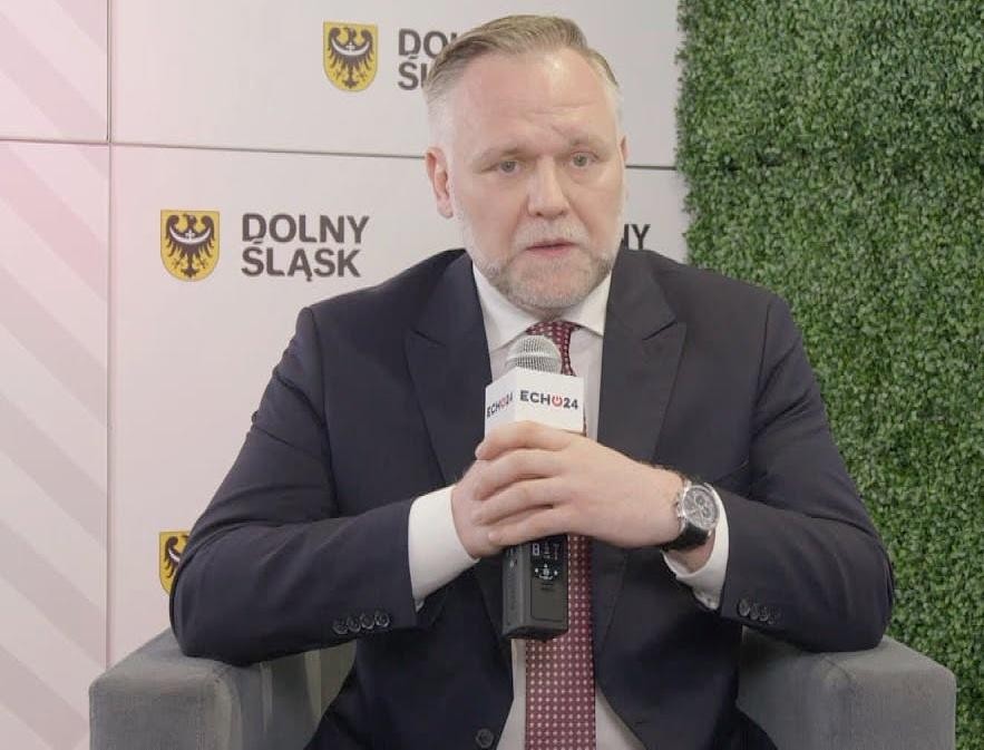 Dawid Jackiewicz podczas wystąpienia publicznego, z widoczną gestykulacją, w profesjonalnym otoczeniu.