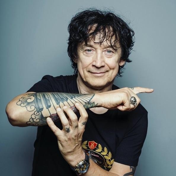 Jan Borysewicz dynamicznie grający na gitarze elektrycznej podczas koncertu Lady Pank, z widocznymi światłami scenicznymi i elementami zespołu w tle.
