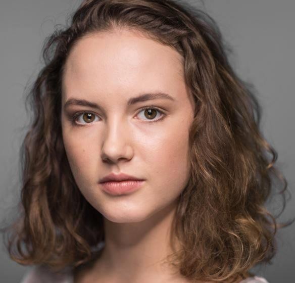 Martyna Byczkowska w dynamicznej pozie aktorskiej, symbolizującej jej edukację w Akademii Teatralnej, w tle zamazane elementy sceniczne.