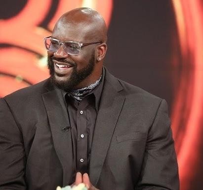 Shaquille O'Neal uśmiechnięty i swobodny, wchodzący w interakcję z fanami lub dziećmi podczas wydarzenia charytatywnego.