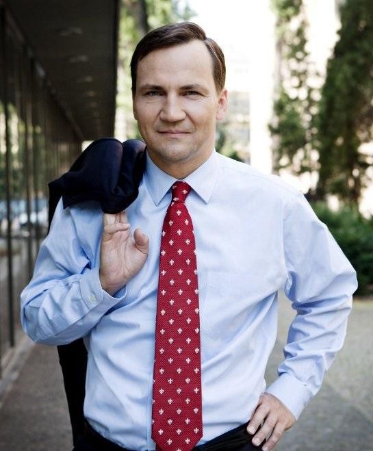 Radosław Sikorski podczas oficjalnego wystąpienia, ubrany w ciemny garnitur, z poważnym wyrazem twarzy.