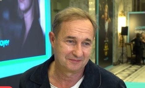 Spokojny, naturalny obraz domu Marka Kality w Puszczy Kampinoskiej, wtapiającego się harmonijnie w otaczający las, z elementami przyrody i miękkim oświetleniem, sugerujący ustronne schronienie.