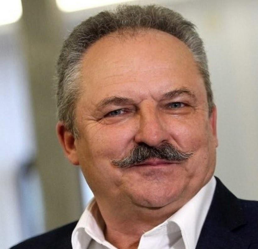 Marek Jakubiak podczas publicznego wystąpienia, dynamicznie gestykulujący, na tle wydarzenia politycznego lub biznesowego.