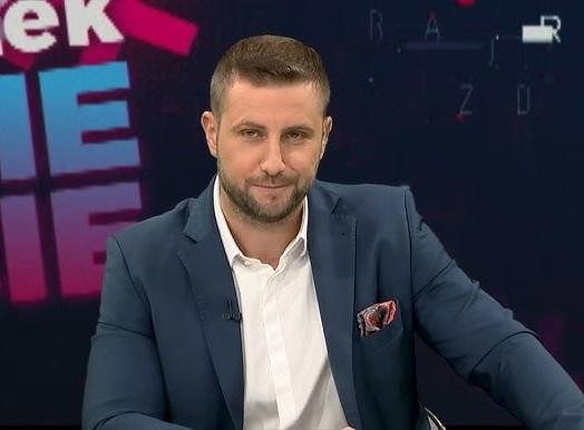 Miłosz Kłeczek w studio telewizyjnym, z dynamiczną ekspresją twarzy, odzwierciedlającą jego styl prowadzenia programów.