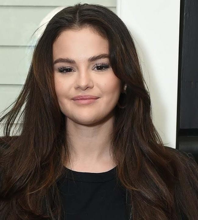Selena Gomez, uśmiechnięta, podczas aktywności charytatywnej lub promująca markę Rare Beauty, z naturalnym światłem podkreślającym jej zaangażowanie.